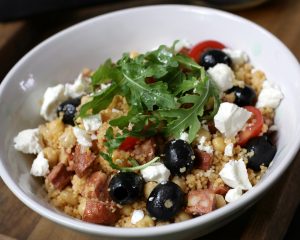 Bowl of couscous with rocket, feta cheese, sausage chunks and olives